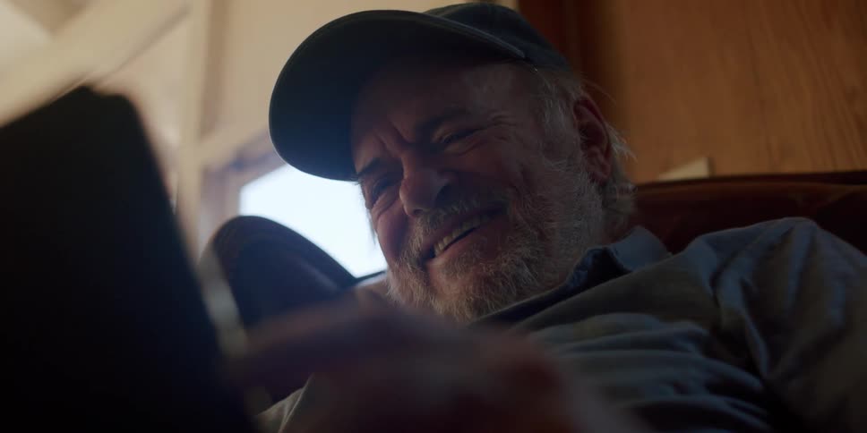 An elderly man holding a tablet and laughing at it