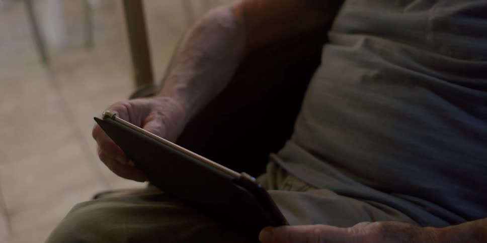 Elderly man sitting in an armchair uses a tablet