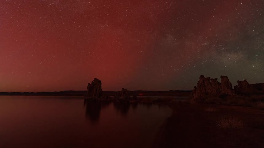Night sky over a serene lake with a reddish hue illuminating the stars and the milky way while tufa formations rise from the water in the foreground