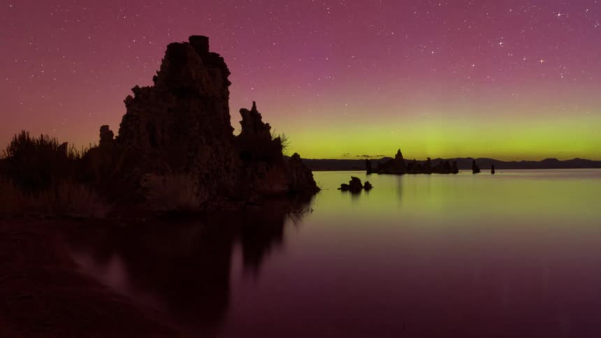 Natural landscape of a lake surrounded by rocks and a starry night sky in shades of green and pink