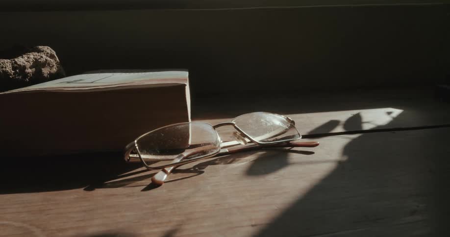 Prescription glasses on a wooden table with sunlight reflection
