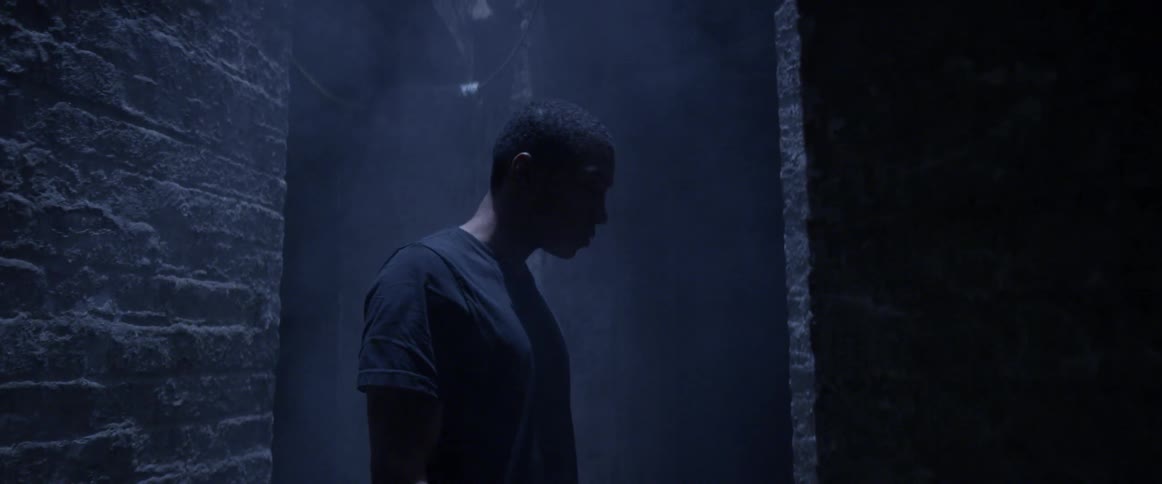 A black man stands in a steamy alley