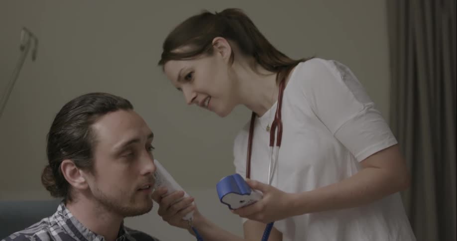 Woman taking mans temperature with ear thermometer