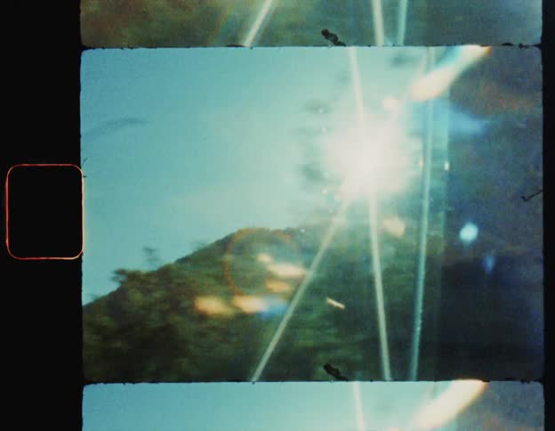 The sun shines over a mountain seen from a moving vehicle caught on vintage film