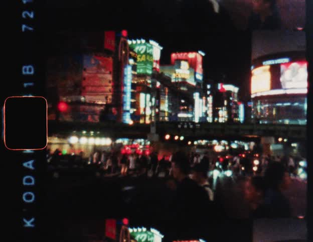 Street in a metropolis with pedestrians crossing and buildings lit up at night