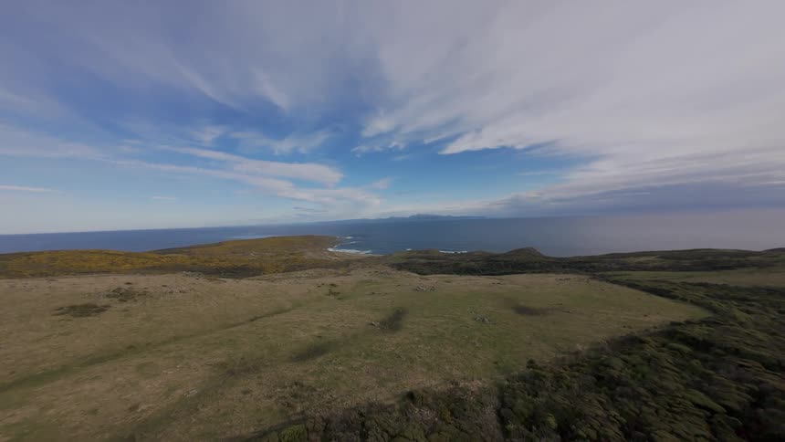 FPV panorama of a long flat expanse surrounded by the sea with dramatic blue sky