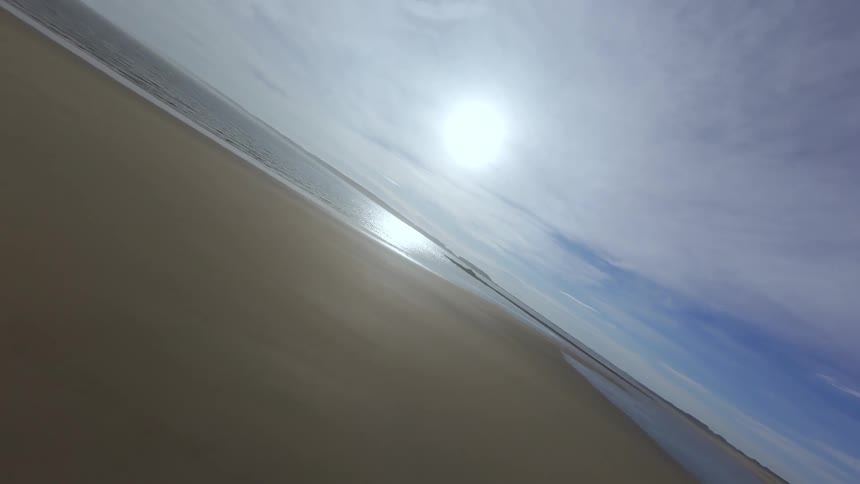 Landscape of a beach with a long stretch of sand and a rocky slope FPV drone weaves through rocks