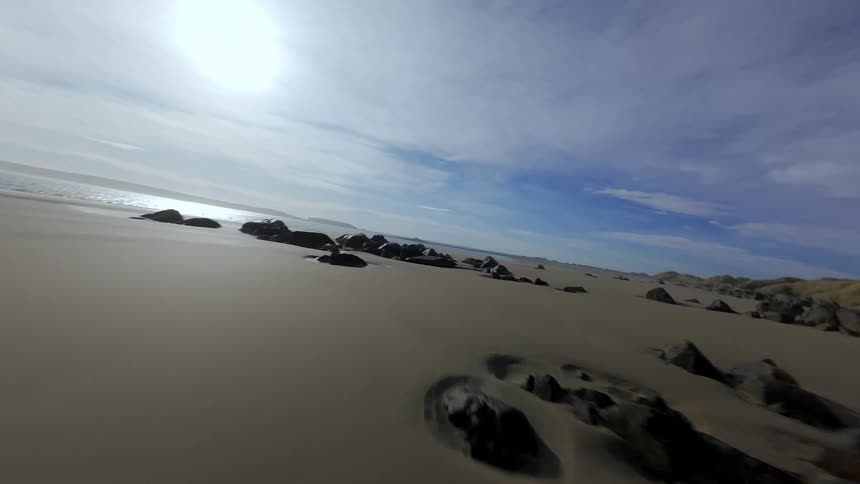 FPV Drone landscape of a beach with a rocky coast and wet sand with stones and the sea in the background with the sun