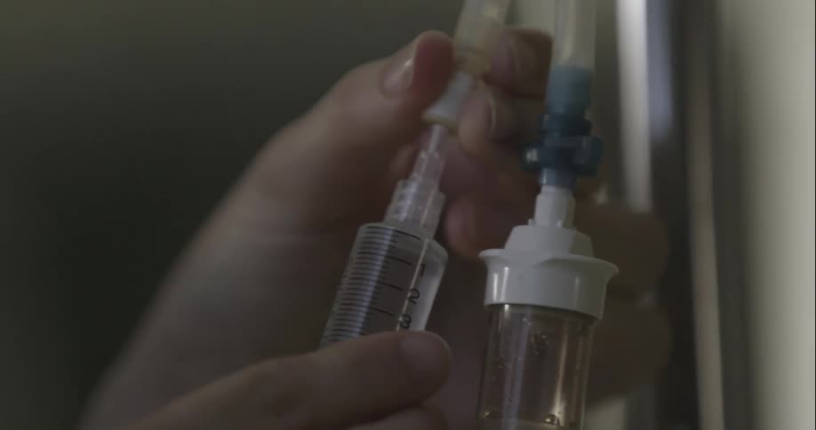 A nurse inserts a needle into a iv bag