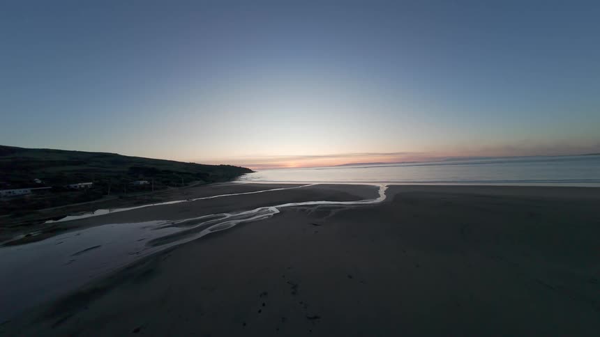 FPV Aerial view of sandy coastline on the edge of a beach at dawn