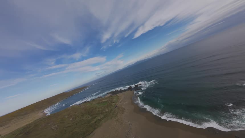 FPV aerial view of a seaside peninsula on a blue sky day