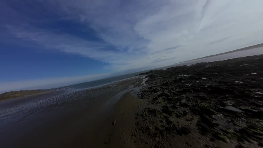 Aerial fpv view of a shore and ocean at the beach across rocks and sand