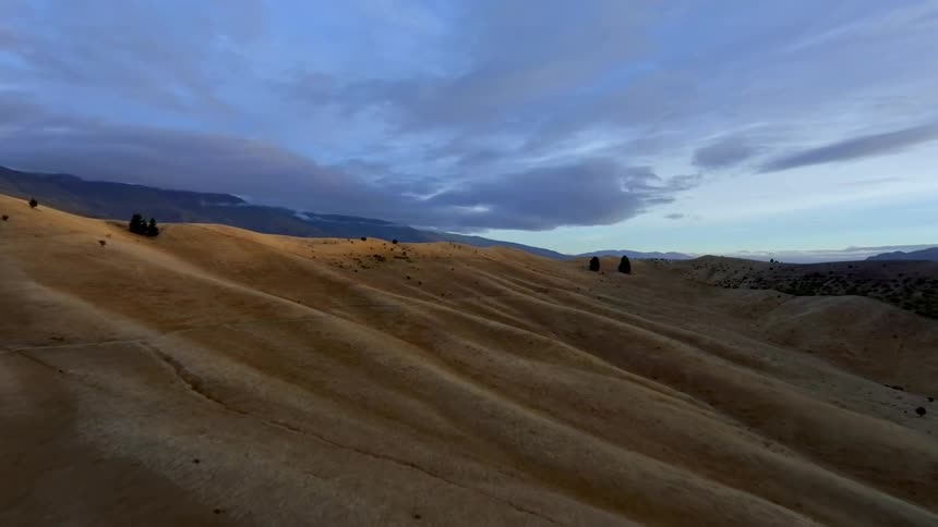Vast landscape with rolling hills covered in dry grass under a wide sky with dramatic clouds
