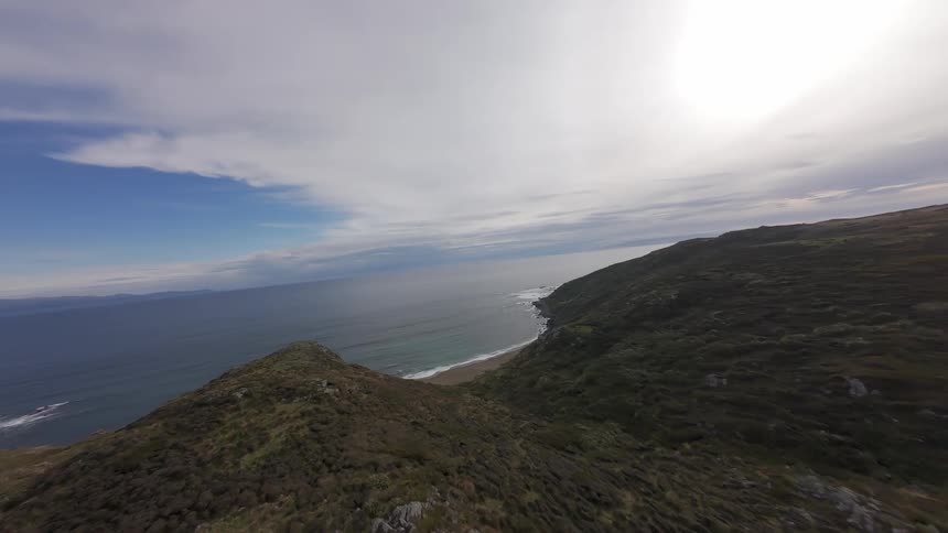 The waves crash against the shore of the green island FPV drone across native trees