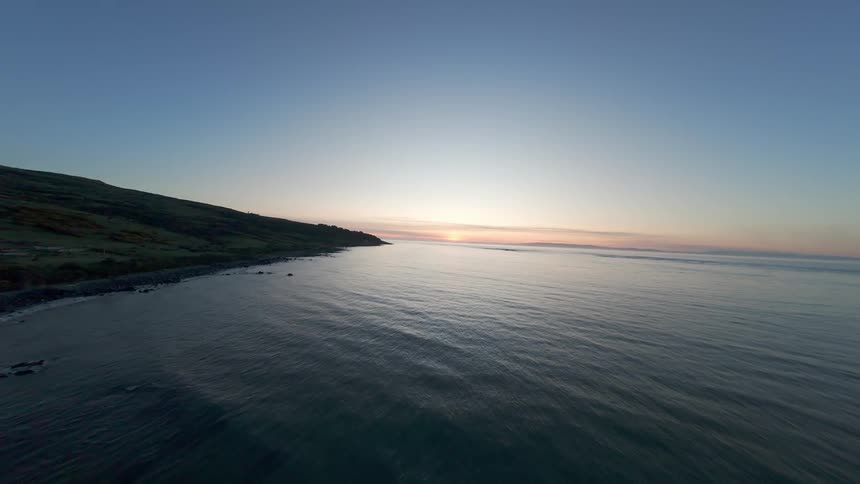 FPV from town on the shore line to the sun setting over the ocean at dusk