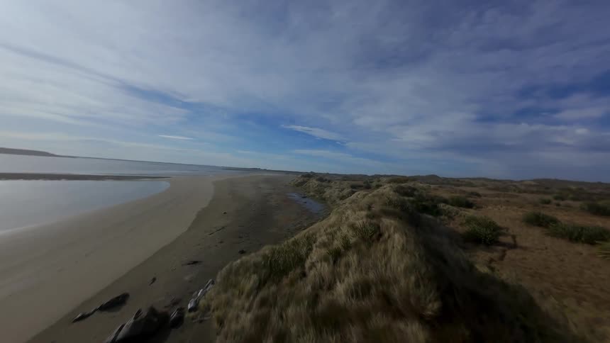 Aerial panorama of a beach with wet sand and FPV flight through small rocks