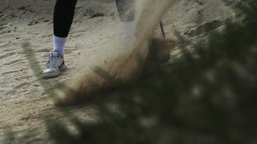 A golfer hits a ball with a sand wedge in slow motion