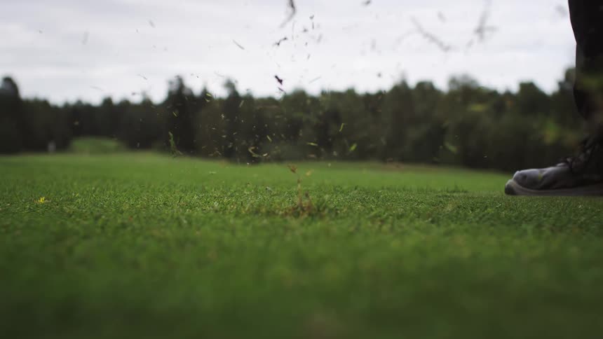 A golf club hitting a ball and pulling out grass from the green