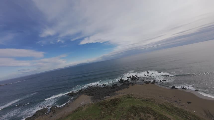 Aerial FPV view of hills  with vegetation on the edge of a beach and blue sea