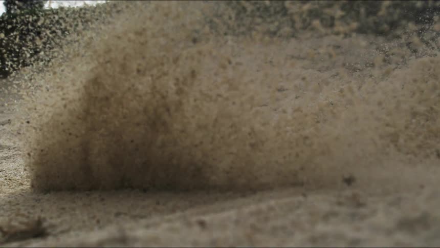 Club hitting a golf ball causing sand from the ground to fly along with it