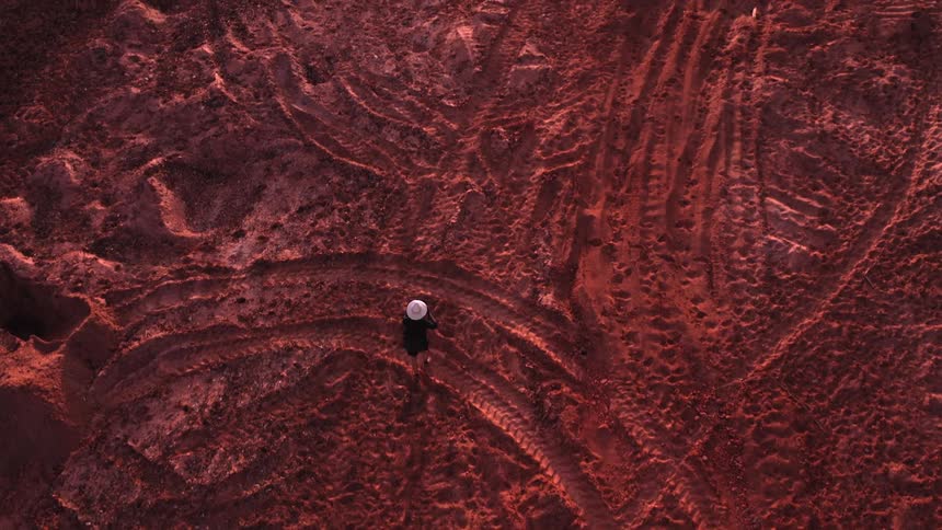 Aerial view of a person wearing a hat walking on red soil