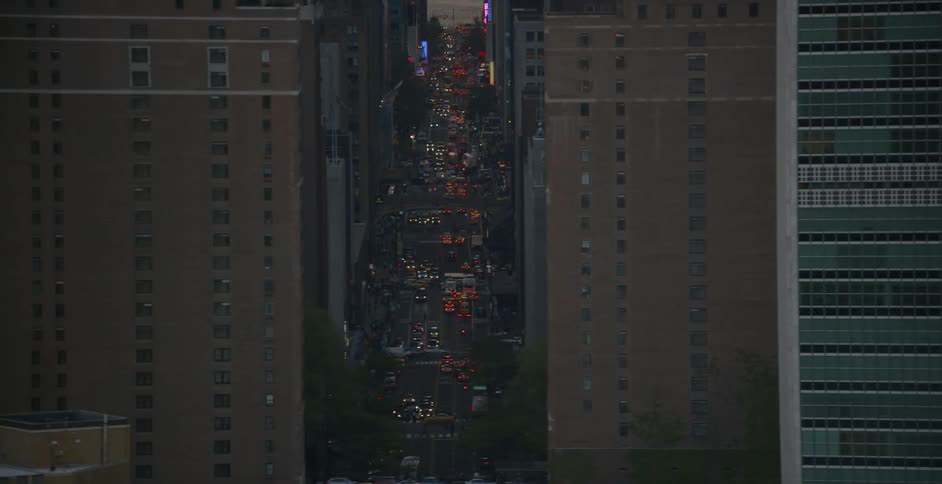 Vehicles drive on a street surrounded by tall buildings