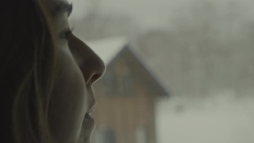 Closeup of a womans profile as she looks through a window at a snowy landscape