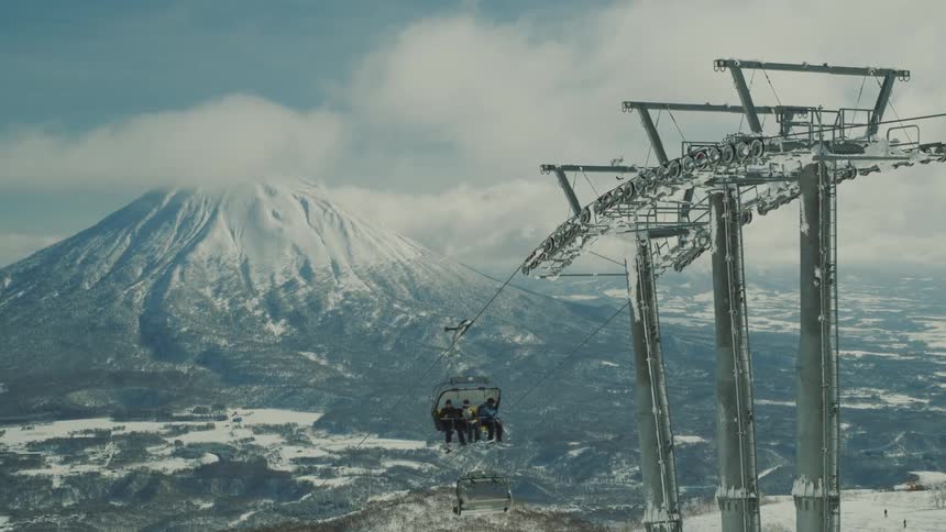 Ski lift with passengers against snowcovered mountains and cloudy sky