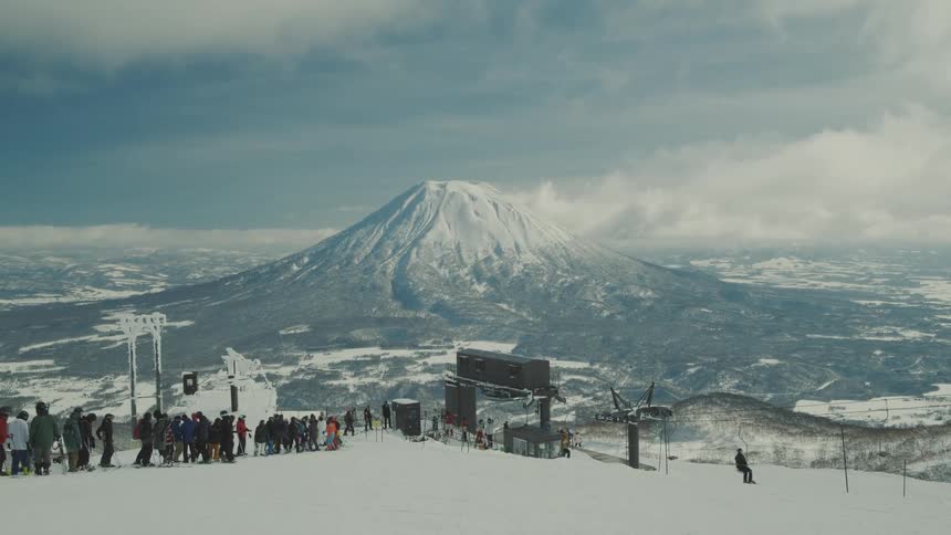Group of people standing in a line and snowboarding through snowy mountains