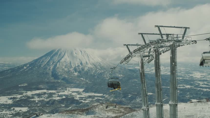 A cable car with several carts passing along the cables in a snowy region with a large mountain in the background