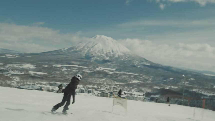 Person snowboarding down a hill with a snowcovered mountain in the distance