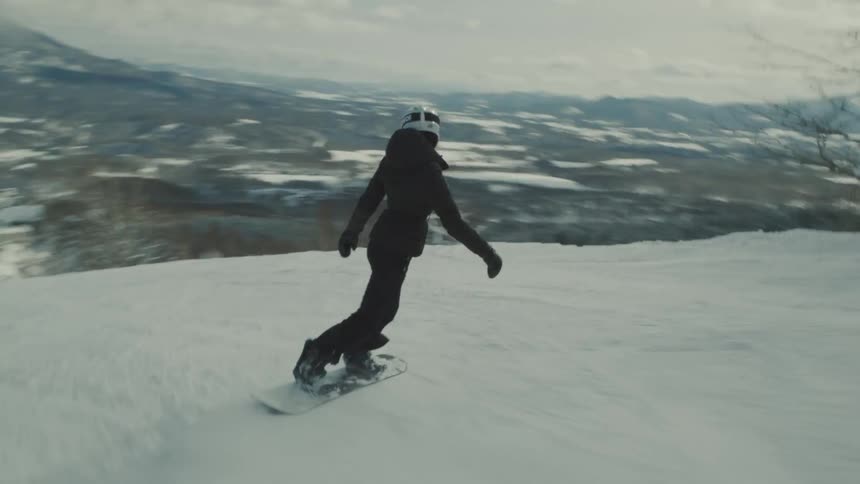 Person wearing a helmet adventuring down a snowboard on a snowy mountain slope