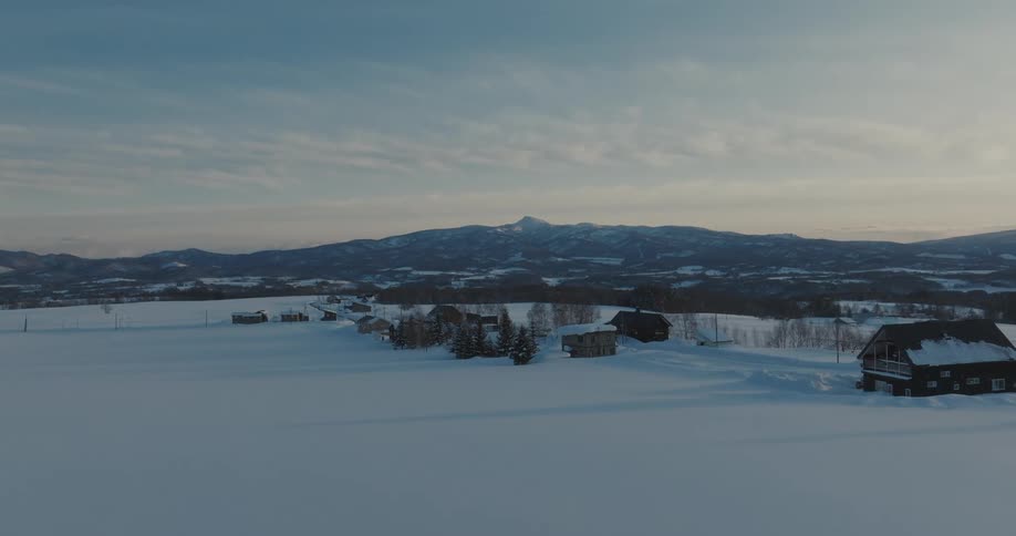 A snow covered landscape with a small village in the valley overlooking a mountain peak against a blue sky