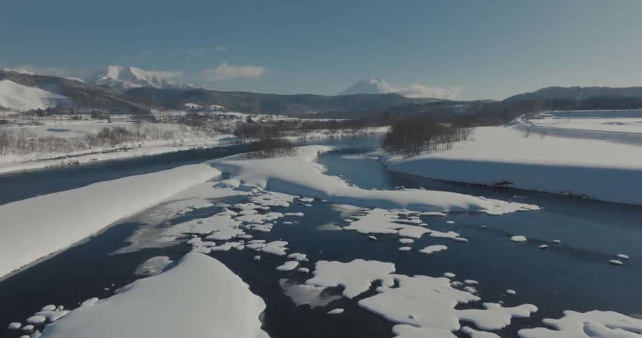 Aerial view of a winter landscape with a river cutting through snowcovered banks and mountain peaks in the distance