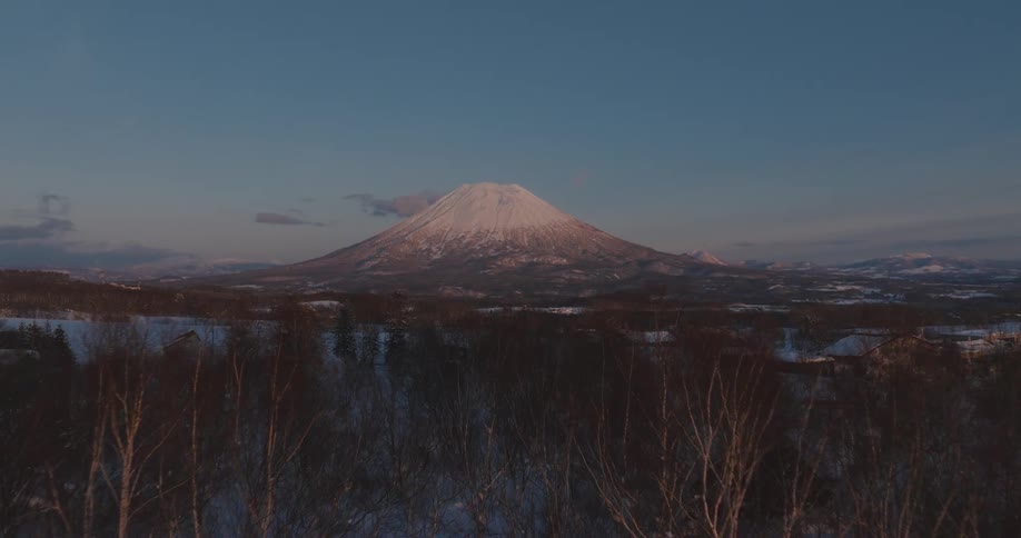 A snow covered mountain likely a volcano under a clear sky at dusk