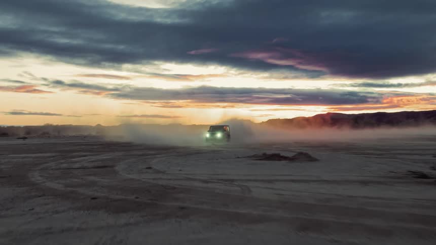 A car is driving in a sandy area and is raising a lot of dust wherever it goes