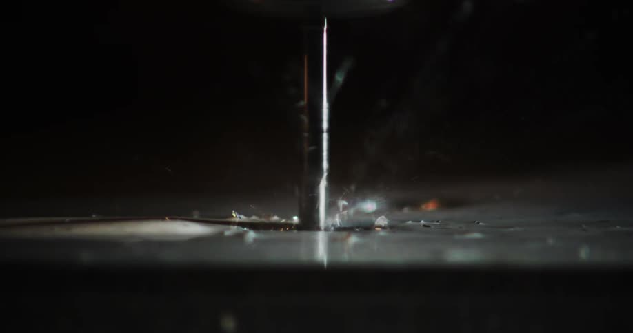 A rotating industrial machine is drilling a metal surface and throwing a lot of metal shavings to the sides