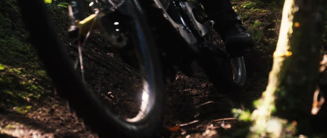 Zoom-in on mountain bike's tires turning on loamy terrain with dirt flying