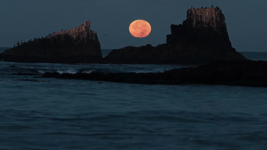 A time lapse of ocean waves and the moon setting behind canyons