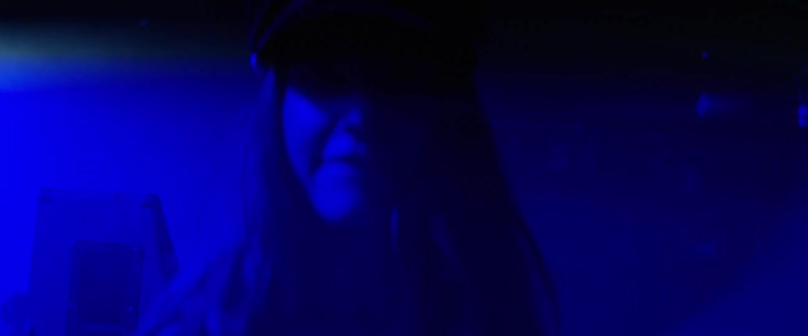 A woman with a hat is in a nightclub with blue lights flashing in the room and she is dancing and spinning