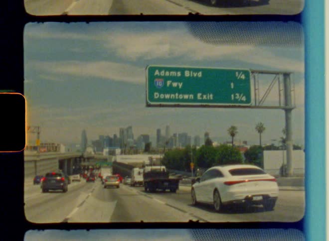 Several cars driving on a multilane asphalt highway and there is a green sign at the top left corner