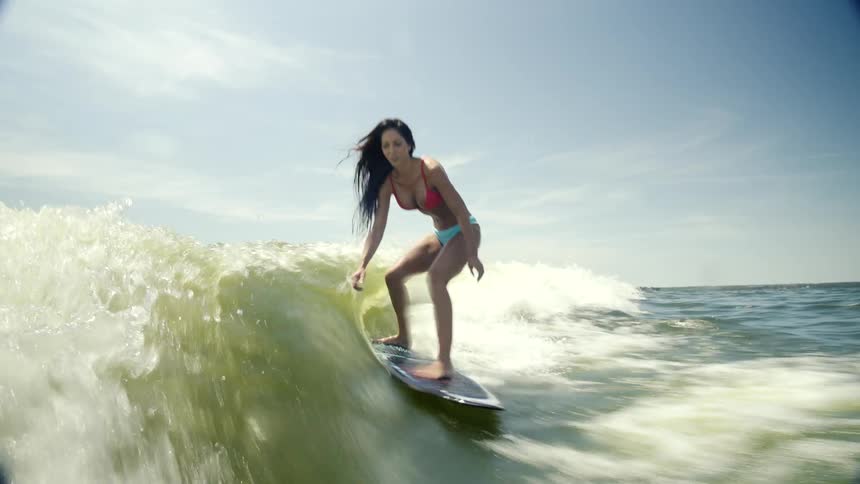 A woman in a pink bikini is surfing a wave and she is doing tricks while surfing and has a smile on her face