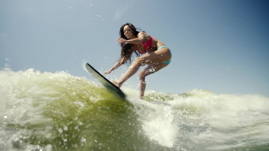 A woman in a red top is surfing a wave using a dark blue surfboard