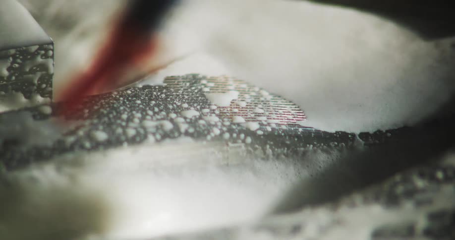 Extreme close up of a metal surface in CNC machine with foam and water passing through