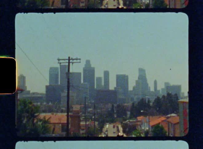 Street view looking down a hill with residential buildings with the skyline of a city in the background