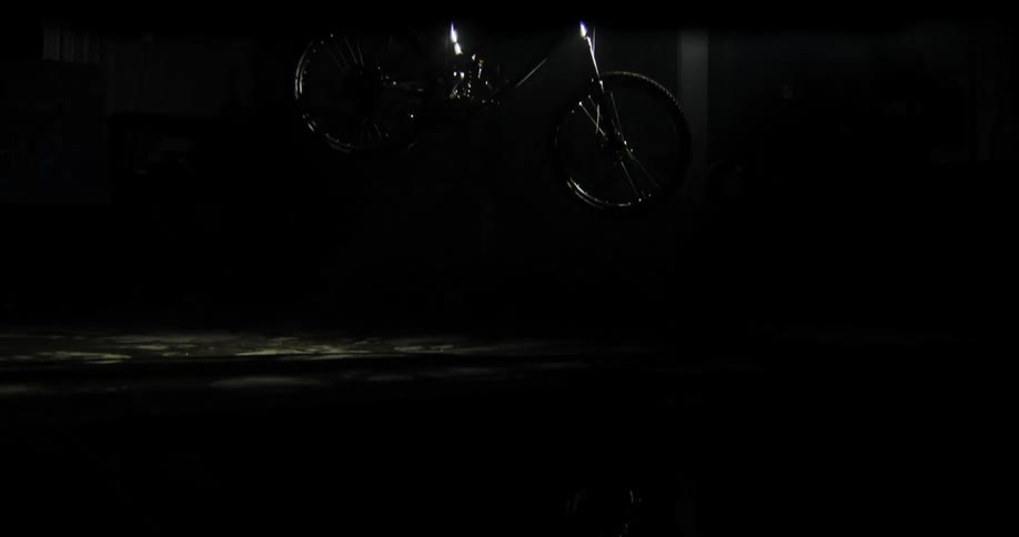 Silver bicycle hanging by a chain from the ceiling in a dark room