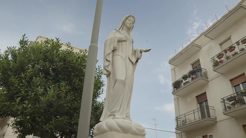 The statue of a woman stands outside an apartment building on a summer day
