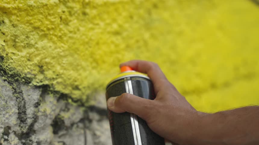 Hand holding a can of spray paint and graffitiing a wall