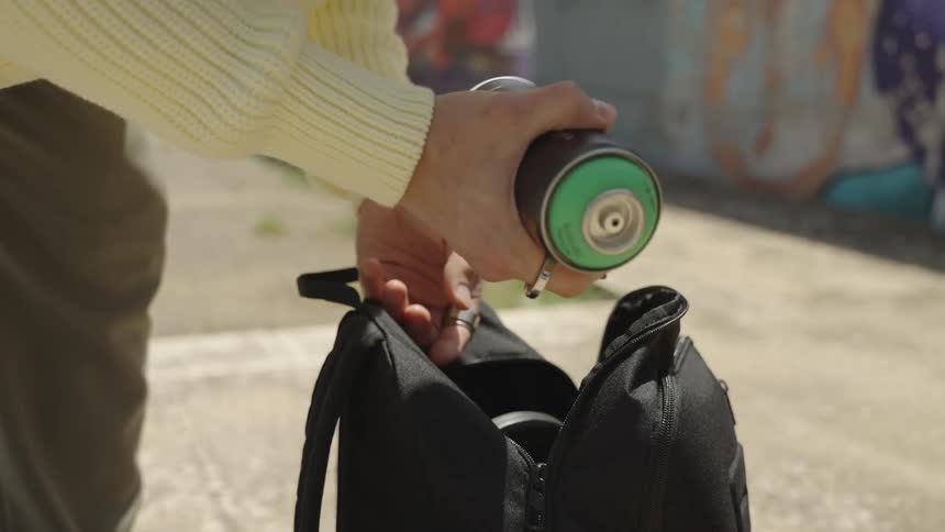 A person holding a green spray paint can in their hand taking it out of their backpack