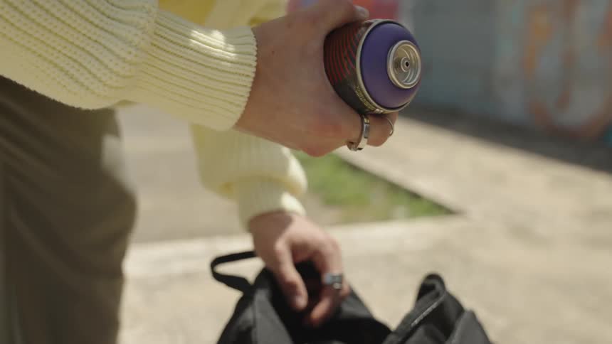 A person holding a spray paint can in their hand taking it out of their backpack